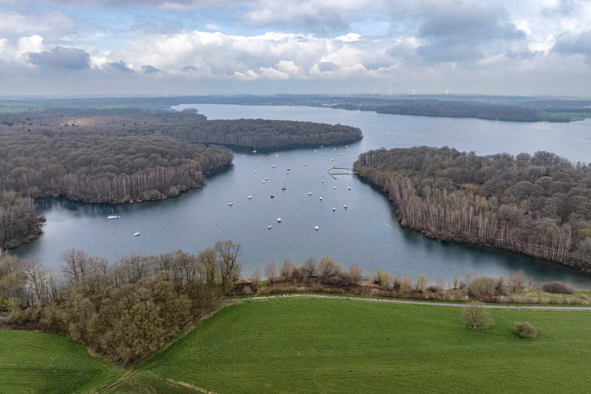 Vue aérienne des lacs de l’Eau d’Heure avec voiliers, forêts environnantes et rives boisées.