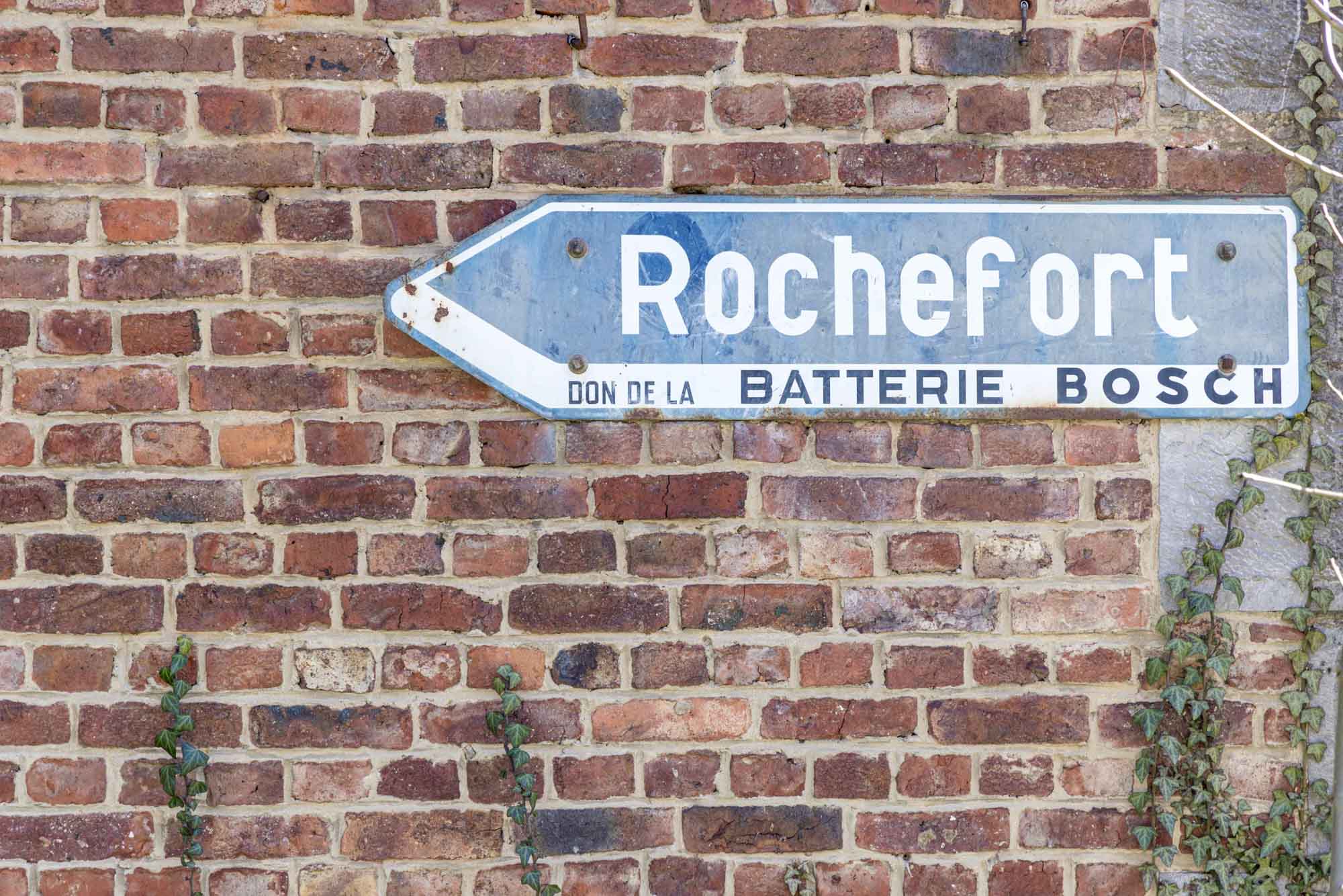 Panneau bleu indiquant Rochefort fixé sur un mur en briques anciennes.