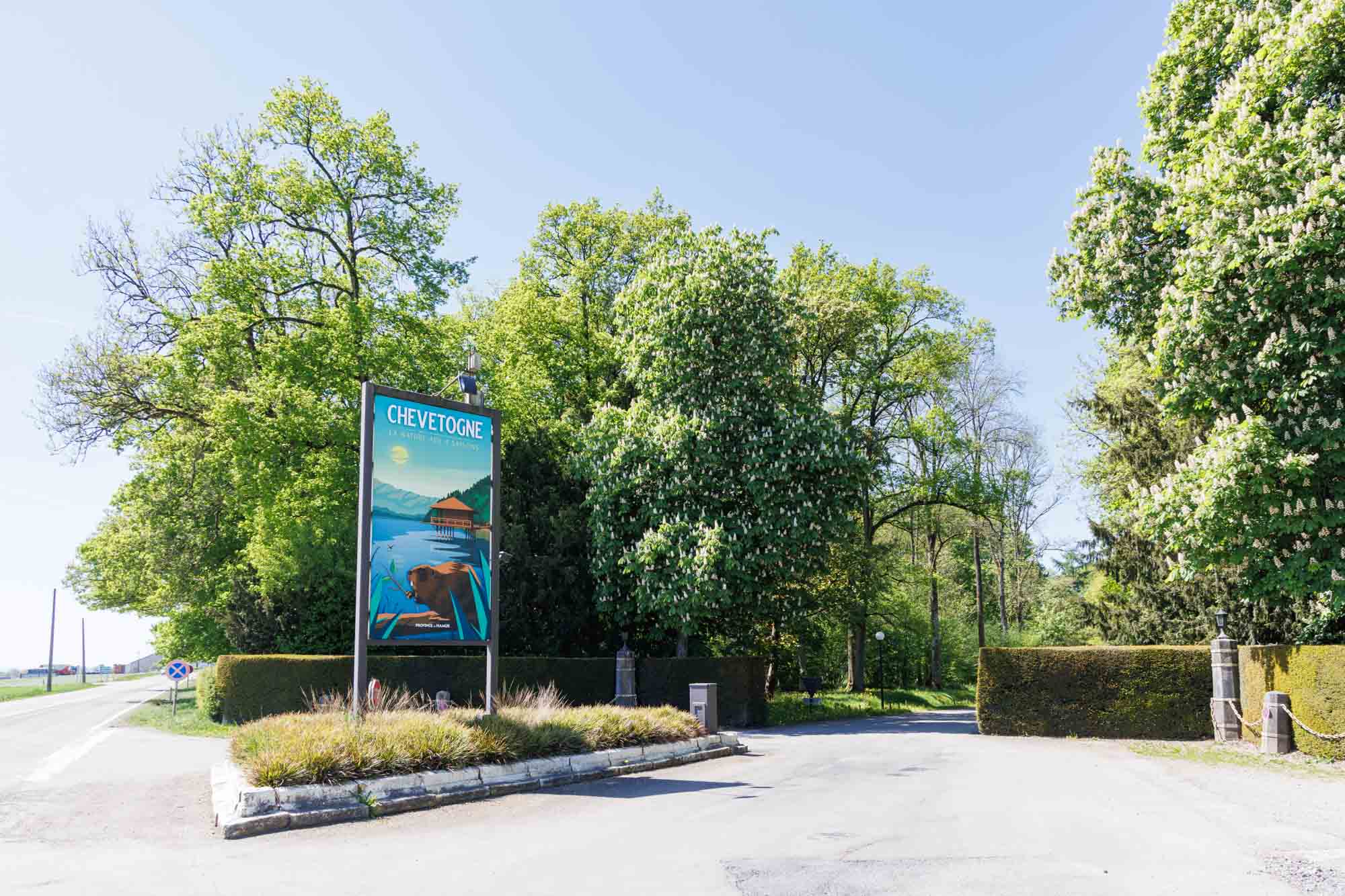 Panneau et entrée du domaine de Chevetogne bordés d’arbres et de haies verdoyantes.