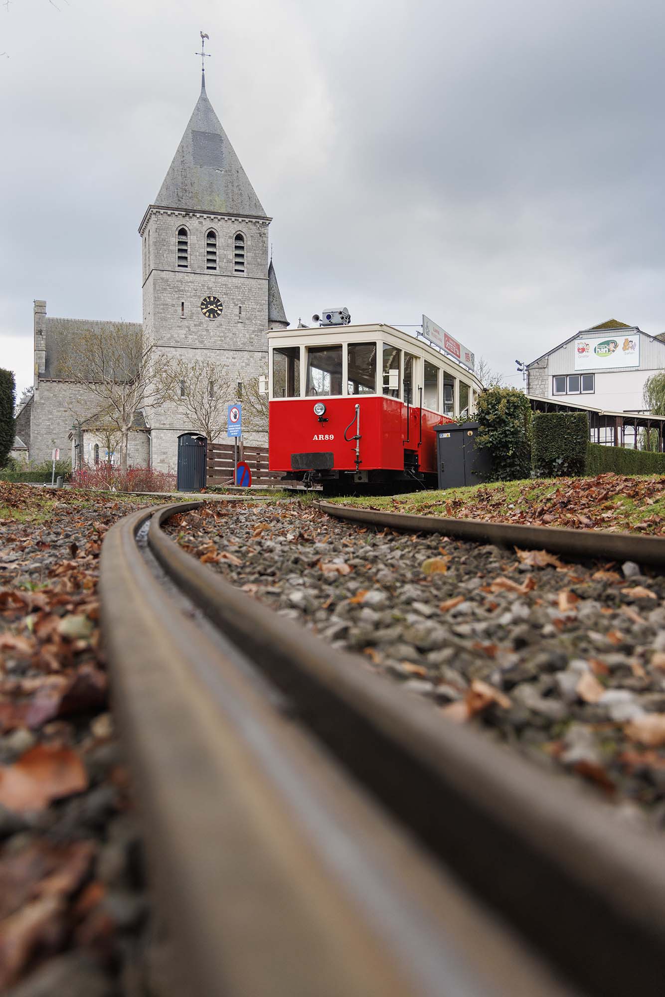 Tram touristique rouge à Han-sur-Lesse devant l’église du village, par temps couvert