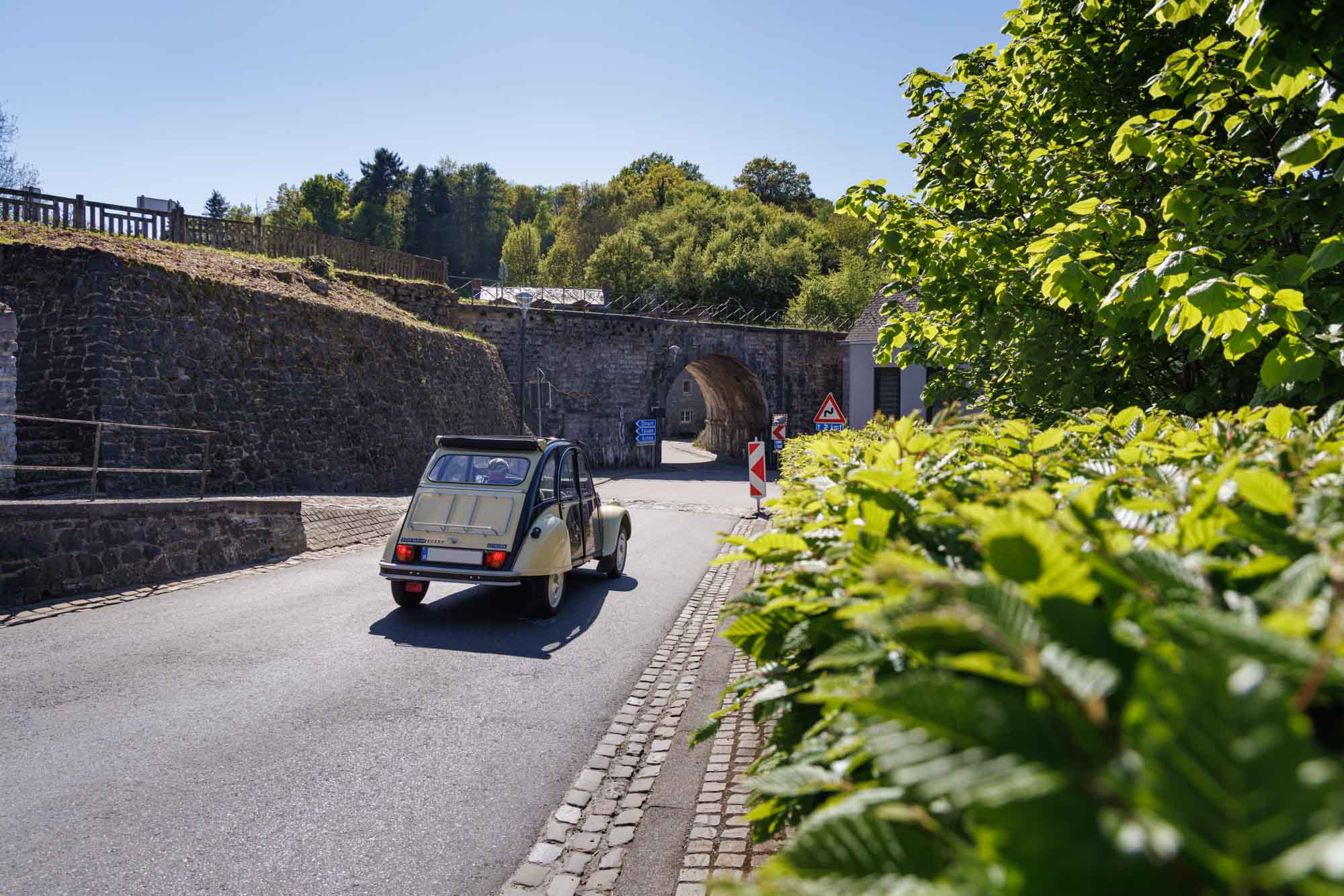 Sosoye avec 2CV roulant vers un passage voûté bordé de verdure